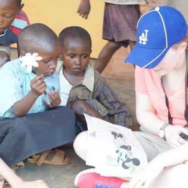 A woman in a blue baseball cap reads to interested young children sitting around her. One holds a flower.